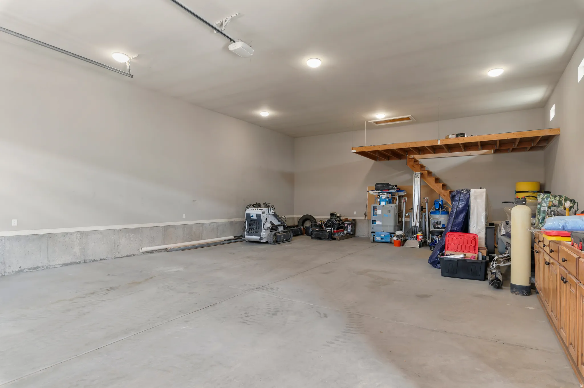 Interior of detached spacious garage featuring a concrete floor, built-in wooden cabinetry, recessed lighting, and an overhead storage loft with wooden stairs