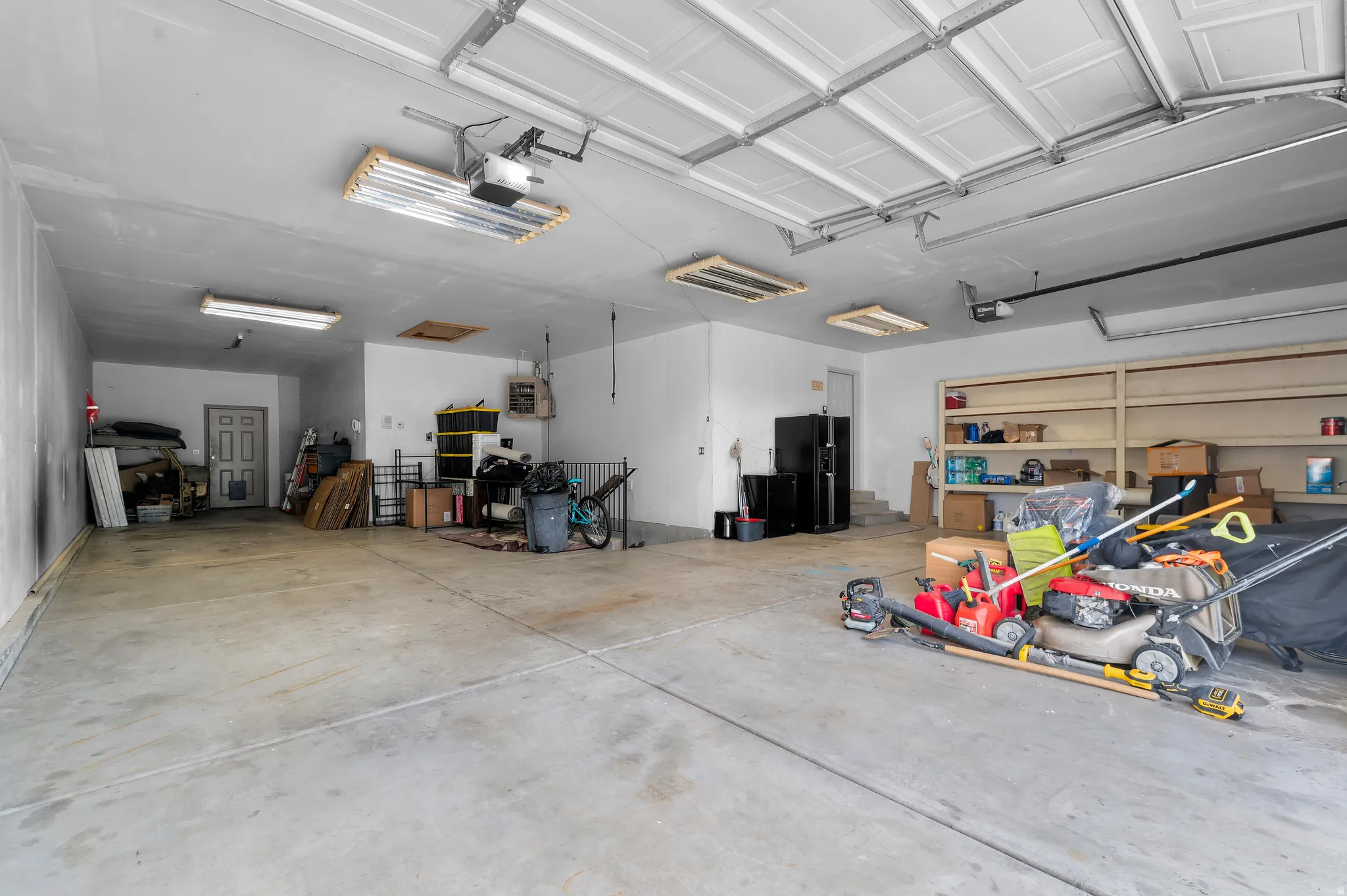Concrete flooring, multiple overhead fluorescent light fixtures, overhead garage door system, white painted walls, built-in shelving