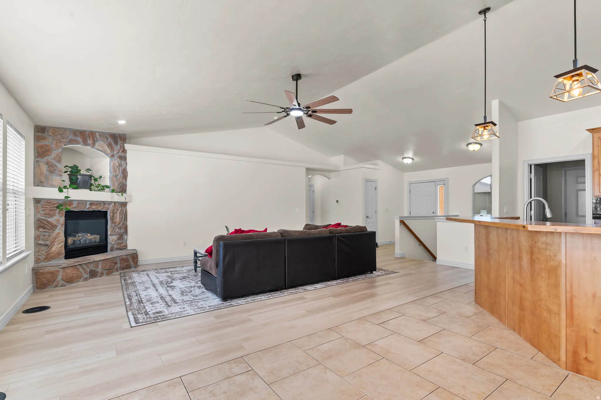 Vaulted ceilings, a stone-clad fireplace, wood-finish flooring, and recessed lighting enhance this living area