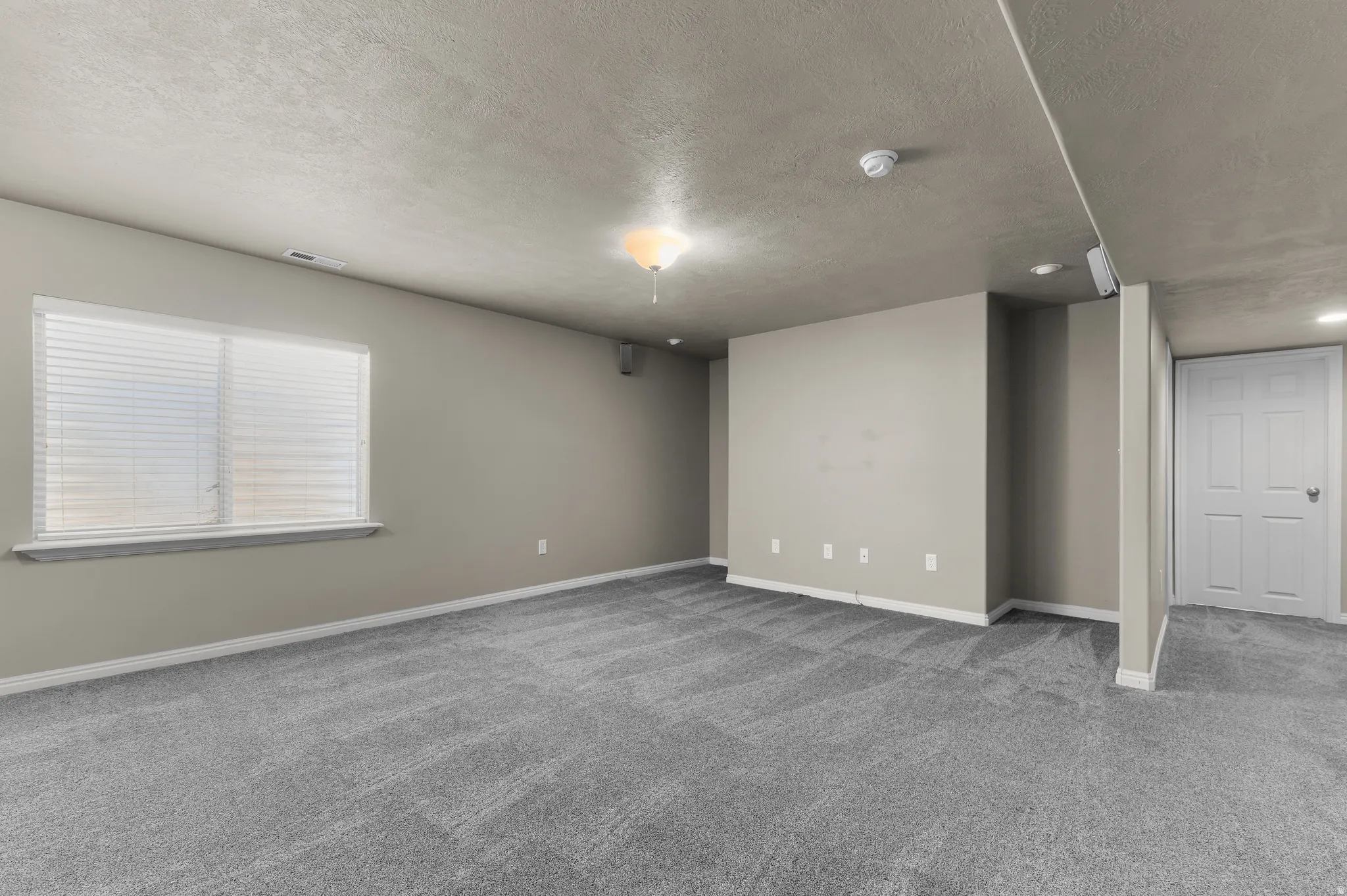 Expansive room featuring plush gray carpeting, neutral-toned walls, and a recessed window with blinds