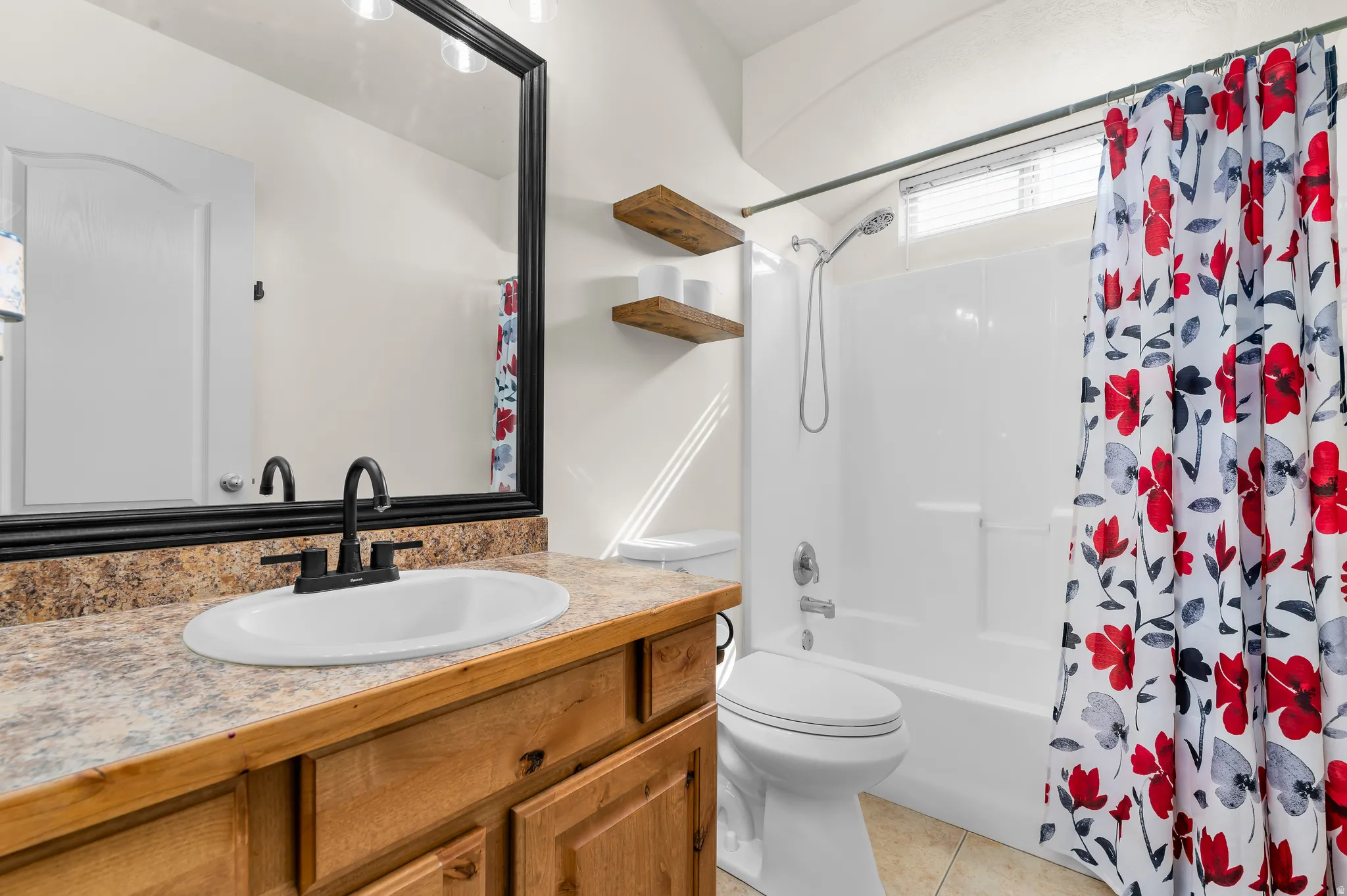 Vanity with natural wood-finish cabinetry, a black framed mirror, and a white tub with shower fixture