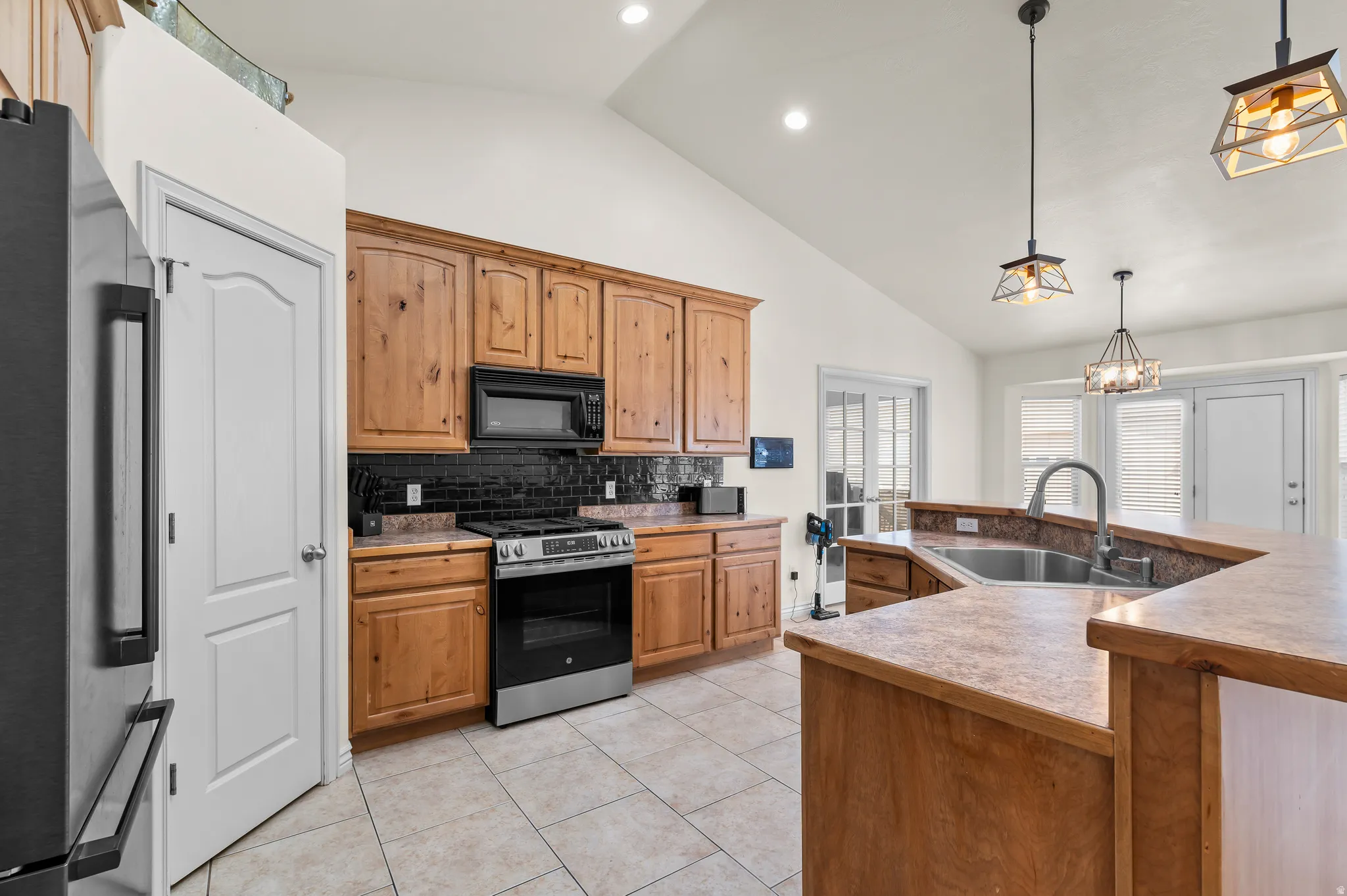 Kitchen featuring vaulted ceilings, recessed lighting, wood cabinetry, stainless steel appliances, and a tile backsplash