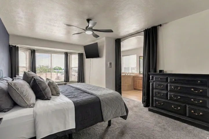Bay window, ceiling fan, arched doorway, wall-mounted television, and carpeted flooring