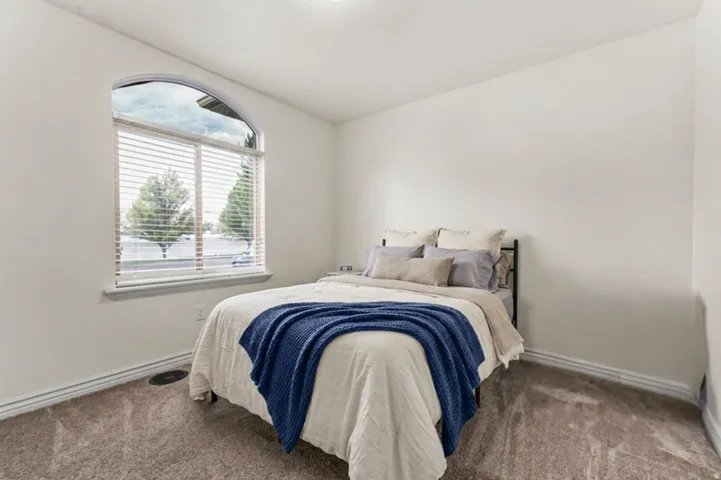Arched window with blinds, white walls, and carpeting