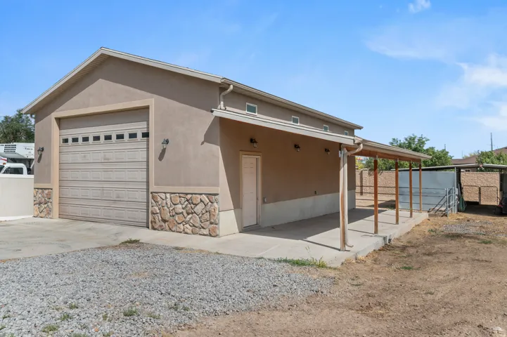 Detached Garage. Stucco exterior with stone veneer accents, large garage door with upper window panels, covered concrete patio, multiple exterior light fixtures, and a covered side entrance door