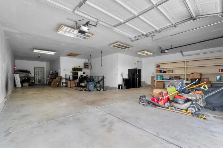 Concrete flooring, multiple overhead fluorescent light fixtures, overhead garage door system, white painted walls, built-in shelving