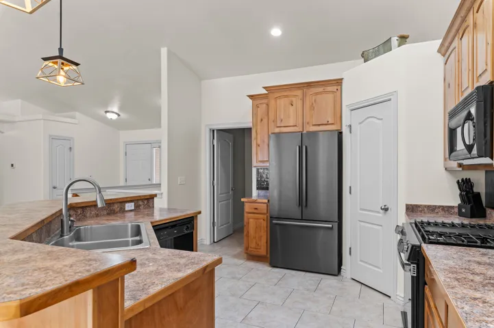 Kitchen featuring a double basin stainless steel sink, wood cabinetry, stainless steel refrigerator, black microwave, and gas range