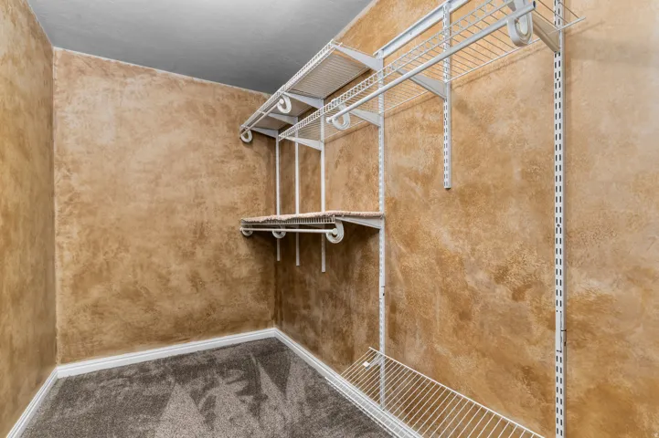 Custom closet organization system with wire shelving and hanging rods over grey carpet flooring