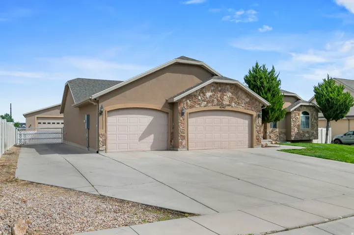 Stucco exterior featuring stone accents, a dual-car garage, and an additional detached garage with an extended driveway