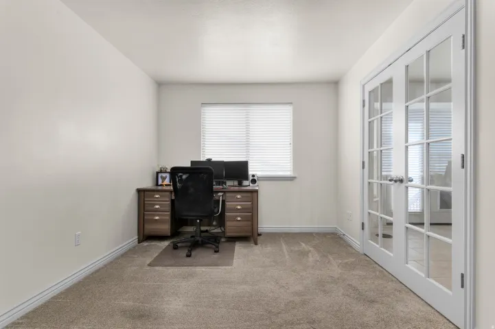 Light-colored walls, window with blinds, light tan carpeting, white baseboards, and white French doors with glass panels