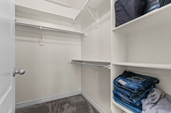 Walk-in closet featuring built-in shelving, multiple hanging rods, and gray carpet