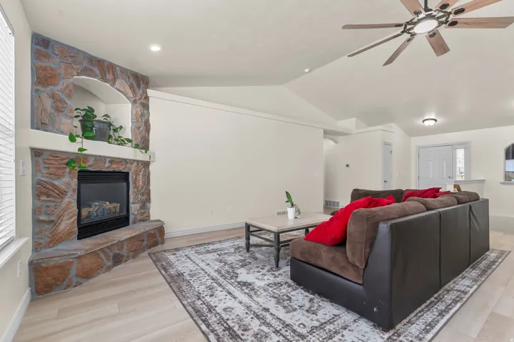 Living area featuring a stone-clad fireplace with mantel and arched niche, wood-finish flooring, a ceiling fan with integrated lighting, recessed lighting, and a white entry door
