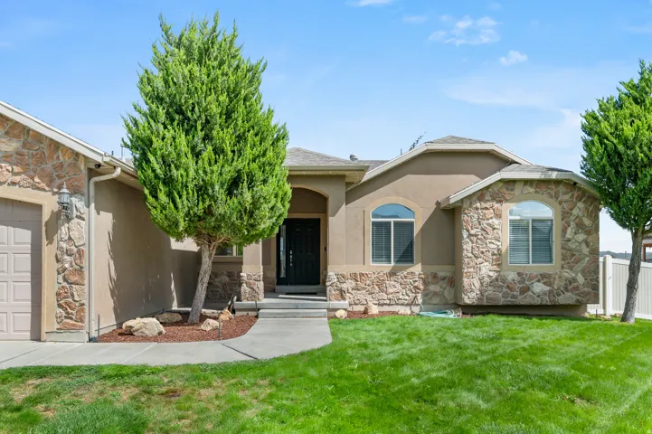 Stucco and stone facade with arched window accents, attached garage, concrete pathway, and manicured lawn