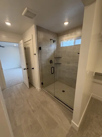 Glass-enclosed shower with dark fixtures and built-in shelving
