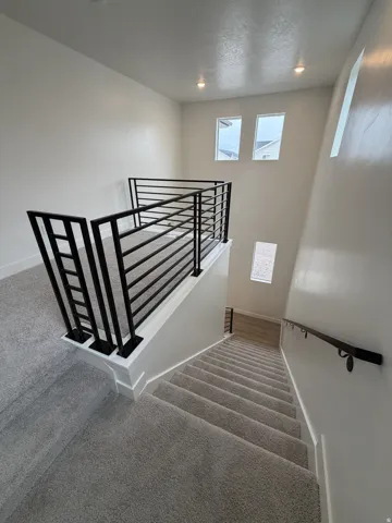 Modern black horizontal iron railings, recessed lighting, and light gray carpeted stairs