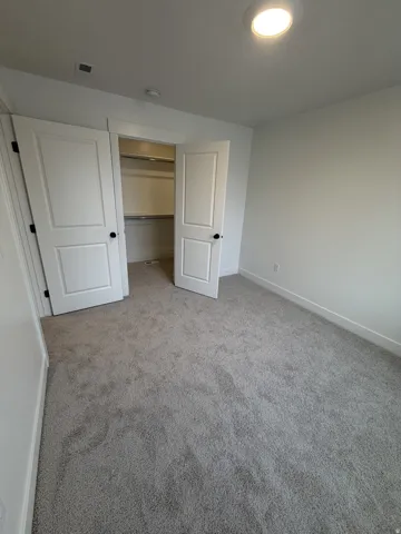 White walls, gray carpet flooring, recessed ceiling lighting, and a closet with white doors