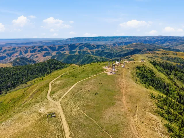 Expansive mountainous terrain with a dirt road, multiple communication towers, and scattered evergreen trees