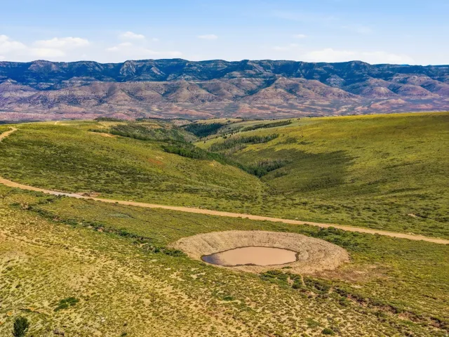 Expansive property featuring varied topography, natural water feature, and a dirt road traversing open terrain