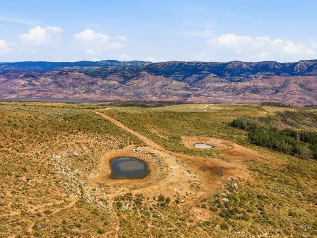 Expansive natural landscape featuring two ponds, unpaved terrain, distant mountain ranges, and scattered vegetation