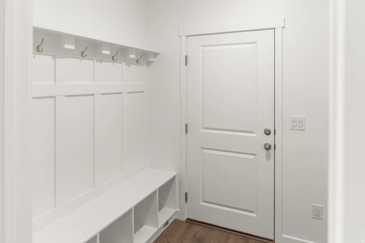 Built-in mudroom bench with storage cubbies and coat hooks, wood-finish flooring, and white paneled door