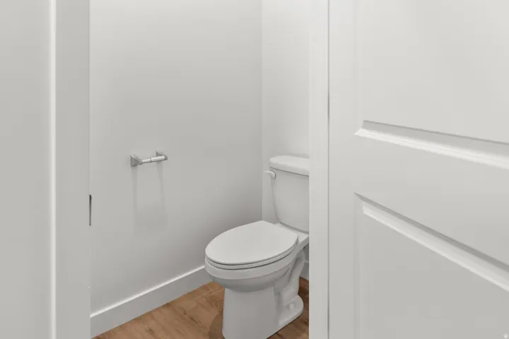 Compact powder room featuring a contemporary white toilet, wood-finish flooring, and a brushed nickel toilet paper holder