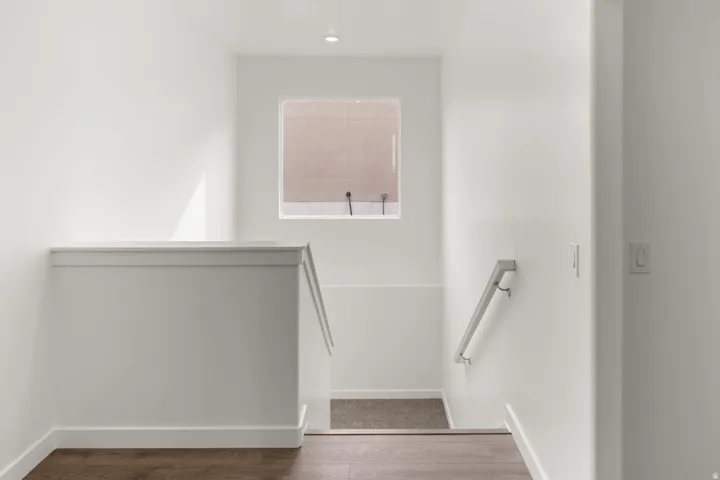 Recessed lighting, wood-finish flooring, half-wall stair railing, window with privacy covering, and a metal handrail