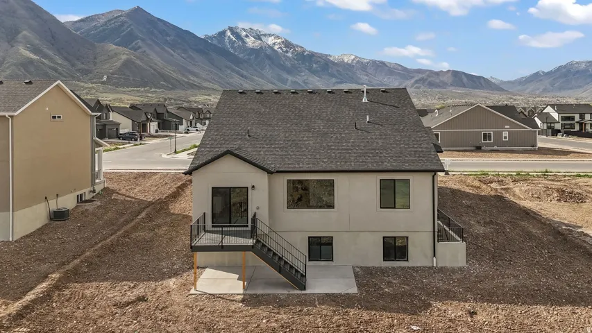 Contemporary stucco exterior with a dark asphalt shingle roof, featuring multiple large windows, a raised deck with dark railings, and a lower-level patio