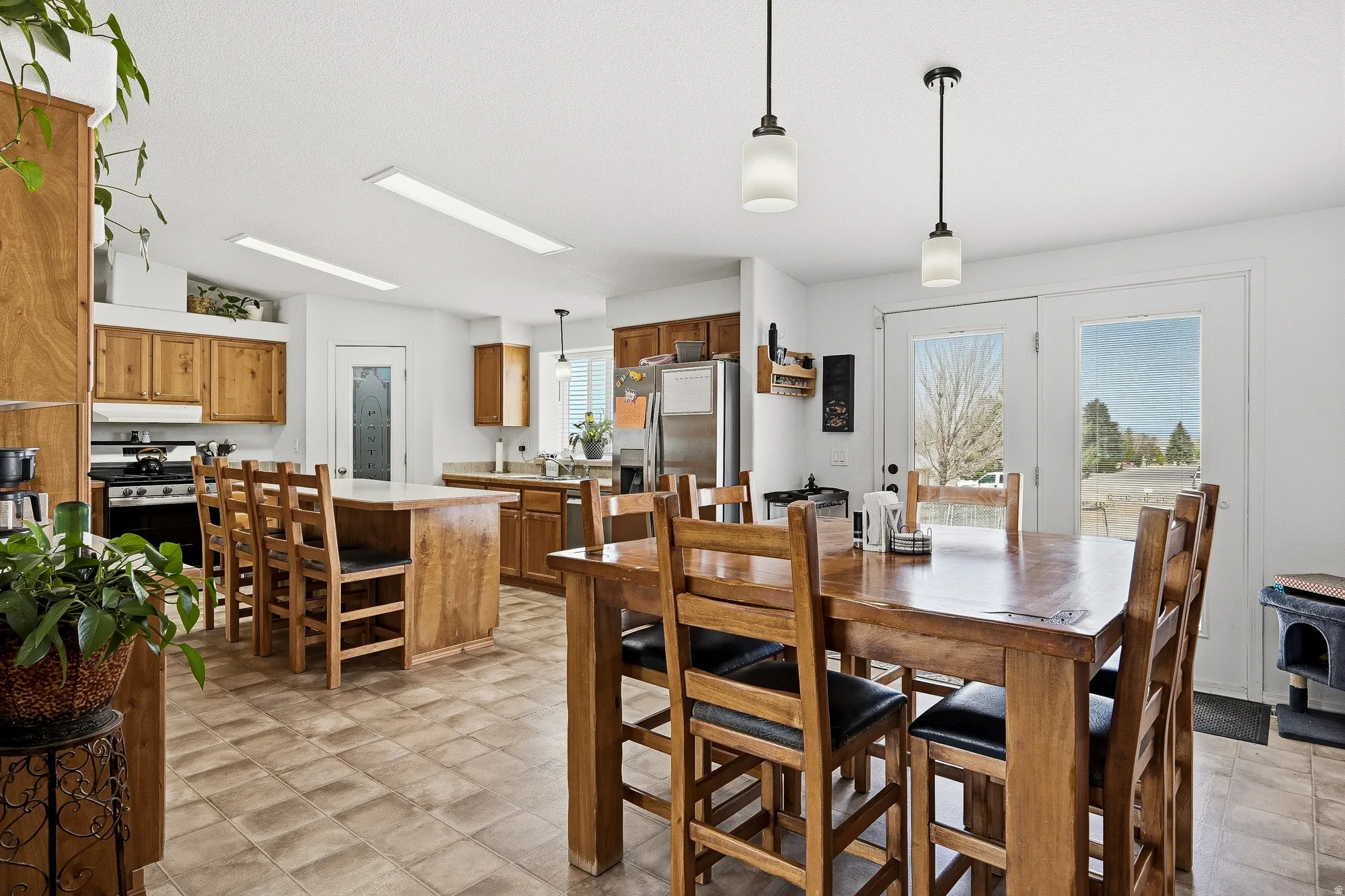 Open-concept kitchen and dining area featuring wood-finish cabinetry, stainless steel appliances, a center island with seating, and tile flooring