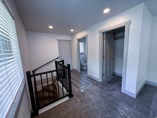 Recessed lighting, window with blinds, wrought iron railing, wood-finish flooring, and gray carpeting