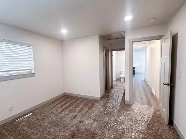 Recessed ceiling lighting, window with blinds, carpeted flooring, white interior doors, and wood-finish flooring in the hallway