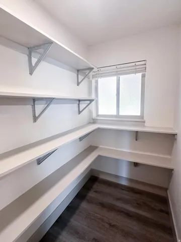 Corner shelving with white finishes, wood-finish flooring, and a window with blinds