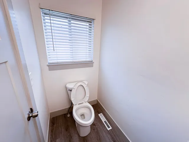 Powder room featuring wood-finish flooring, a white toilet, and a window with blinds