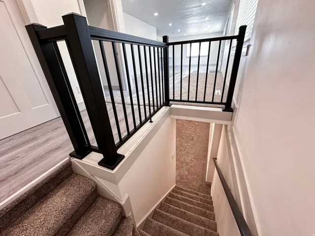 Carpeted staircase with black wrought iron railing and white newel posts