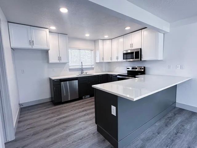 Modern kitchen with two-tone cabinetry, stainless steel appliances, white countertops, and wood-finish flooring