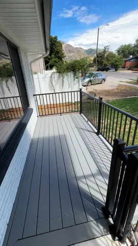 Front porch featuring gray composite decking, black metal railings, white painted brick, and white vinyl siding
