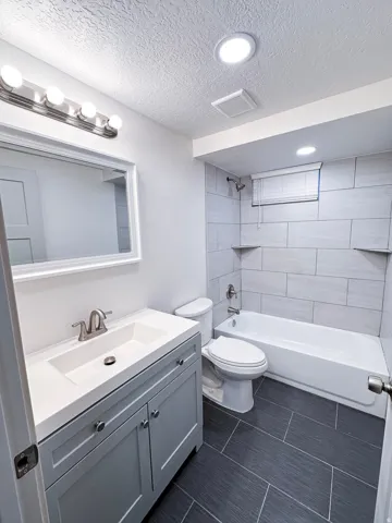 Bathroom featuring a light gray vanity with an integrated sink, brushed nickel faucet, large vanity mirror, and a full-size bathtub with subway tile surround and integrated shelving