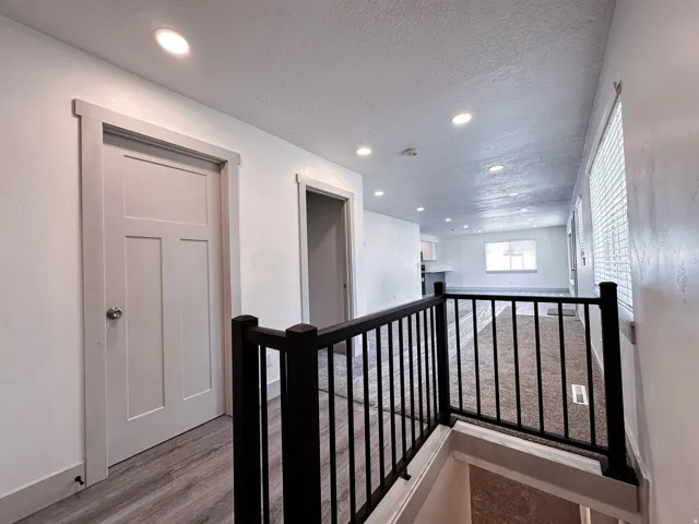 Hallway featuring recessed lighting, wood-finish flooring, and a black wrought iron railing