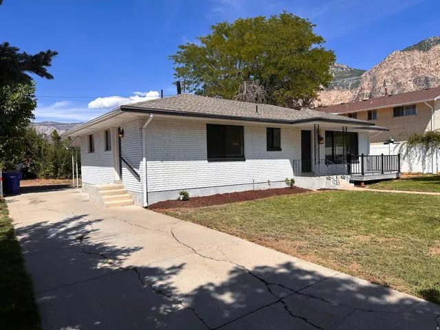 White brick exterior with a dark-shingled roof, featuring a covered porch with black railing, a well-maintained lawn, and a concrete driveway