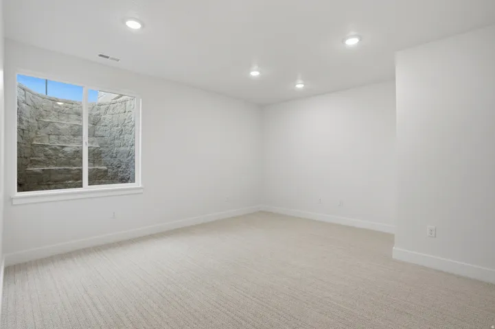 Recessed lighting, light-toned carpeting, white walls, and a window with a stone-finish well