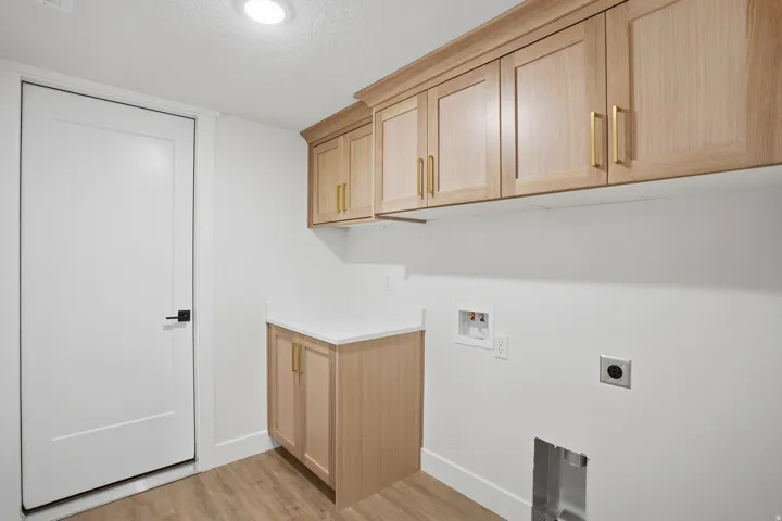 Light wood-finish cabinetry with gold-tone hardware, white countertop, and wood-finish flooring