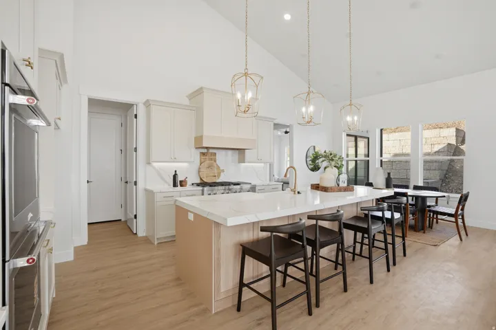 Kitchen featuring a vaulted ceiling, wood-finish flooring, built-in double ovens, and a central island with countertop seating