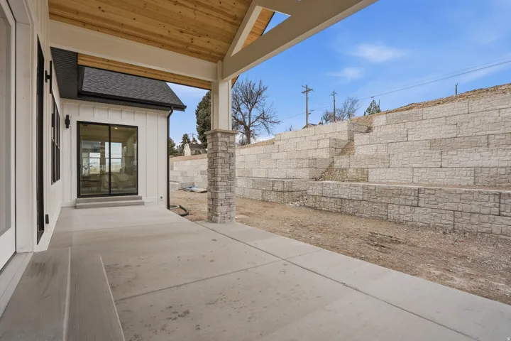Covered patio with a wood-plank ceiling, exposed wood beams, and a stone-clad support column