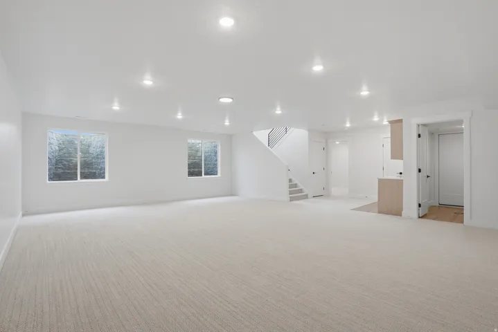 Spacious room featuring light-toned carpeting, recessed ceiling lighting, two windows, and a staircase with an open railing