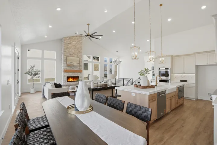 Vaulted ceilings, a stacked stone fireplace with a wood mantel, wood-finish flooring, a kitchen island with stone countertops, and built-in stainless steel appliances