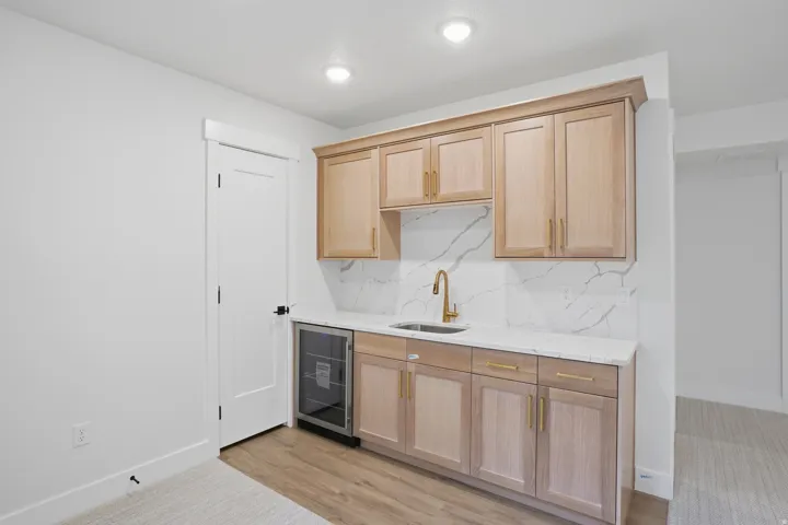 Light wood-finish cabinetry with gold-tone hardware, white countertop, and a white backsplash with gray veining