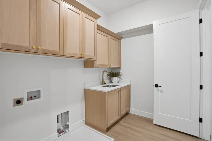 Light wood-finish cabinetry with gold-tone hardware, white countertop with undermount sink, and brass-finish faucet
