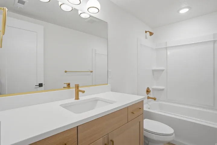 Bathroom featuring a vanity with a white countertop and an integrated sink, gold-finish fixtures, and a white tub with a shower