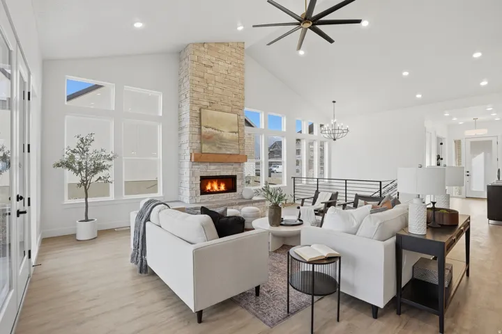 Vaulted ceilings, a stone-clad fireplace with a wood mantel, wood-finish flooring, a contemporary ceiling fan, and recessed lighting