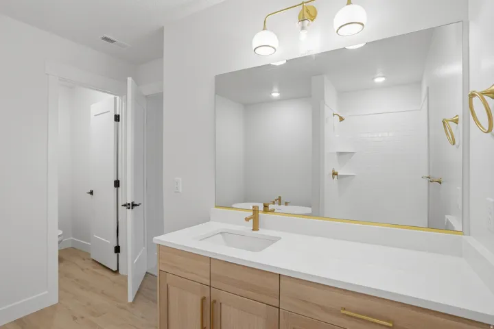 Bathroom with a light wood-finish vanity, white countertop, integrated sink, and brass-finish fixtures