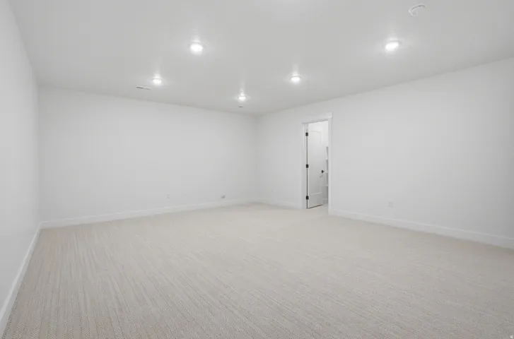 Recessed ceiling lighting, white walls, light-toned carpet, white trim, and a white interior door with black hardware